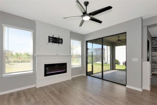 unfurnished living room with light wood finished floors, ceiling fan, a fireplace, and baseboards