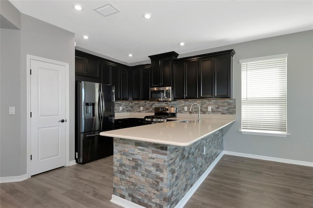 kitchen with a peninsula, light wood-style flooring, a sink, stainless steel appliances, and light countertops