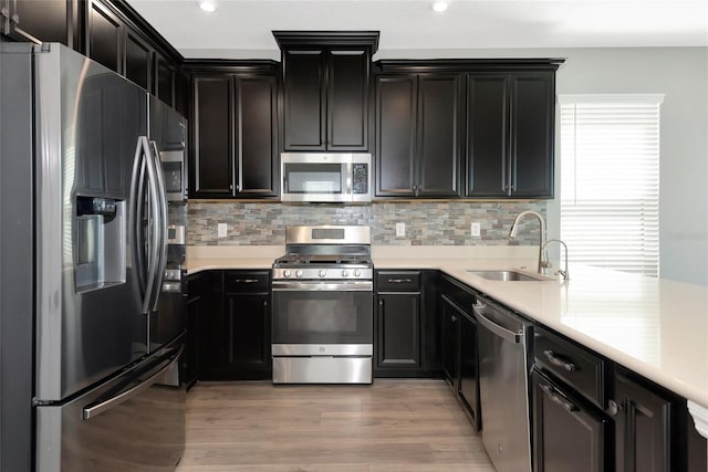 kitchen with a sink, stainless steel appliances, light wood finished floors, decorative backsplash, and light countertops