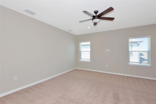 spare room with light colored carpet, baseboards, visible vents, and ceiling fan