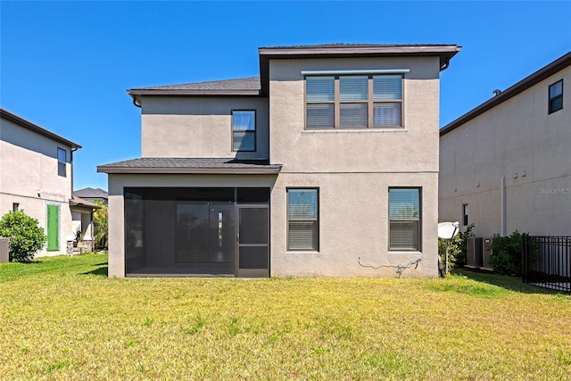 rear view of house featuring a yard, a sunroom, fence, and stucco siding