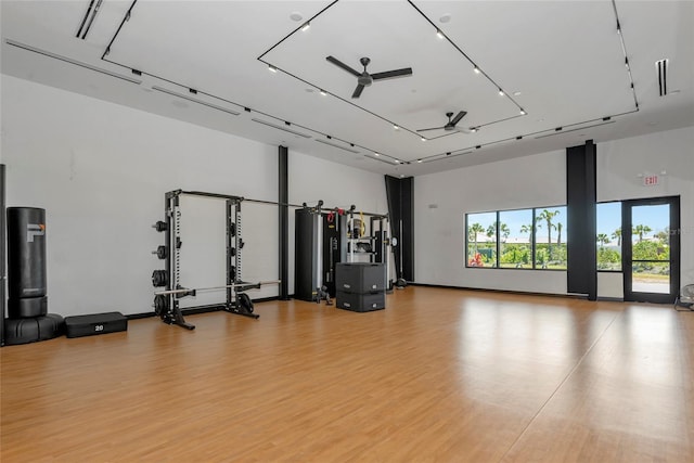 workout area featuring light wood-style floors, a towering ceiling, and a ceiling fan