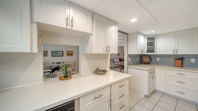 kitchen featuring backsplash, glass insert cabinets, light countertops, light tile patterned floors, and white cabinetry