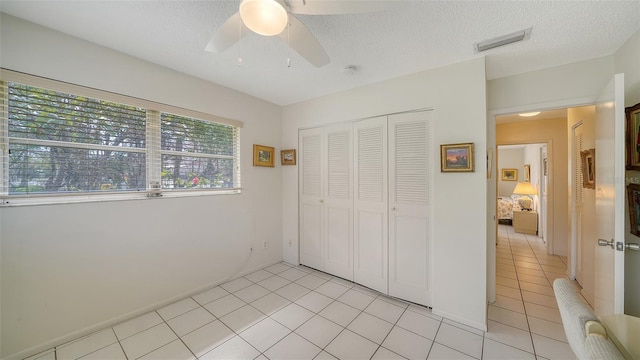 unfurnished bedroom with visible vents, light tile patterned flooring, a closet, a textured ceiling, and a ceiling fan