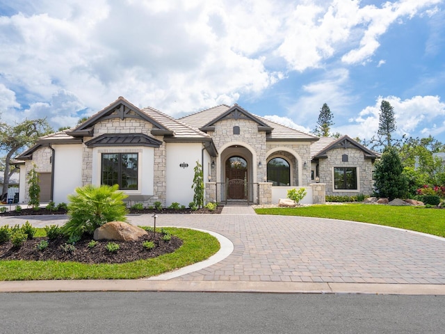 french provincial home with stone siding, curved driveway, a front lawn, and a gate