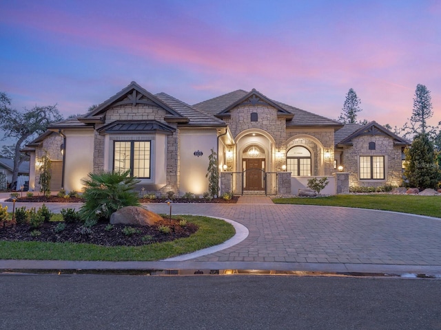 french country home featuring stone siding, stucco siding, decorative driveway, and a gate