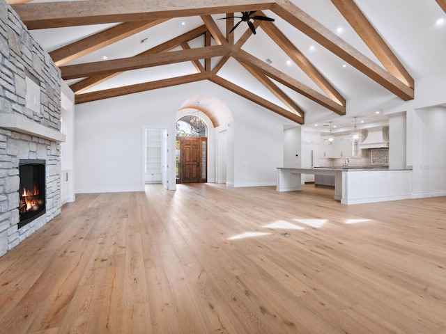 unfurnished living room featuring light wood finished floors, a stone fireplace, high vaulted ceiling, and a ceiling fan