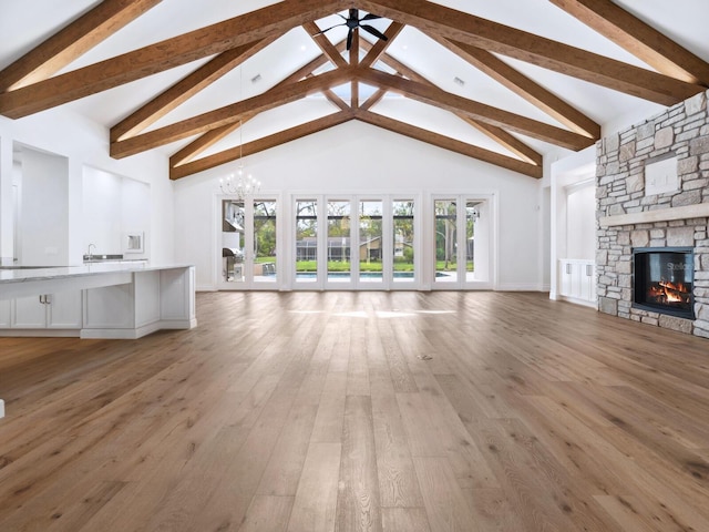 unfurnished living room featuring baseboards, light wood finished floors, high vaulted ceiling, beam ceiling, and a stone fireplace