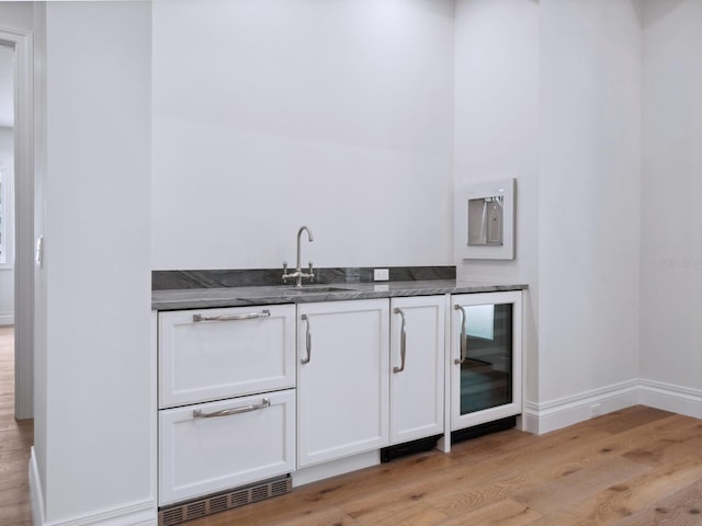 bar featuring beverage cooler, light wood-style floors, baseboards, and a sink