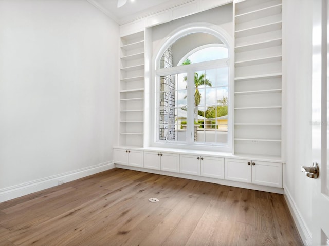 spare room featuring built in shelves, light wood-style floors, and baseboards