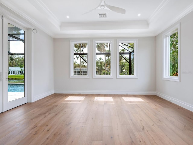 empty room with a tray ceiling, light wood-style floors, visible vents, and crown molding