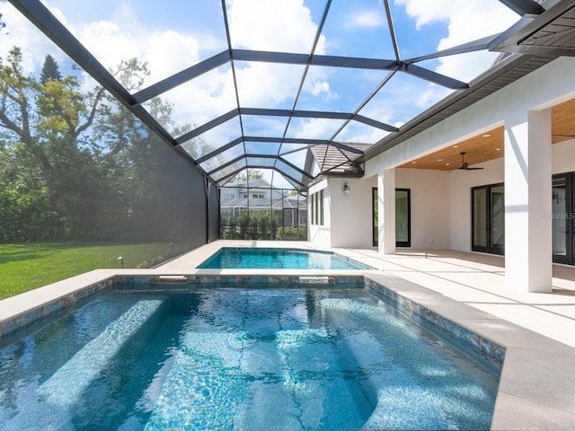 view of pool with glass enclosure, a pool with connected hot tub, ceiling fan, and a patio area