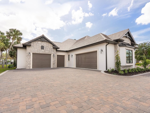 french country style house with decorative driveway, stone siding, an attached garage, and a tiled roof