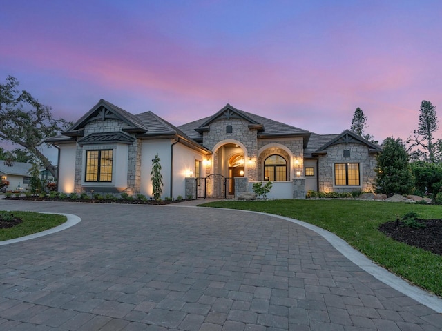 french provincial home with decorative driveway, a yard, stucco siding, and a gate