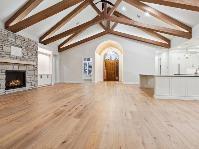 unfurnished living room with light wood finished floors, a stone fireplace, an inviting chandelier, arched walkways, and high vaulted ceiling