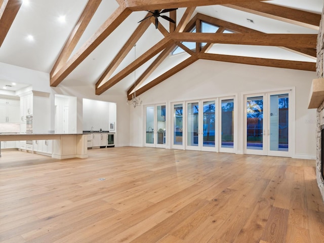 unfurnished living room featuring light wood-type flooring, beam ceiling, french doors, high vaulted ceiling, and a ceiling fan