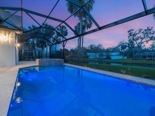 pool at dusk with glass enclosure, a patio area, a lawn, and a pool with connected hot tub