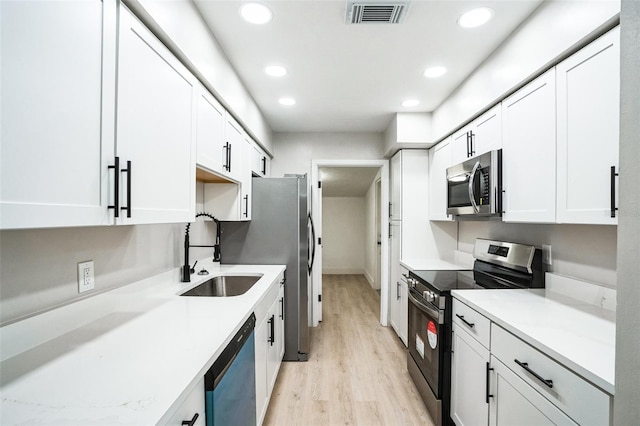 kitchen with stainless steel appliances, visible vents, white cabinetry, a sink, and light wood-type flooring