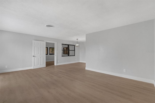 unfurnished room with baseboards, visible vents, wood finished floors, a textured ceiling, and a notable chandelier