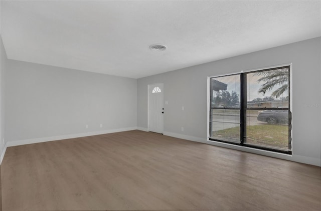 unfurnished living room with a textured ceiling, wood finished floors, visible vents, and baseboards