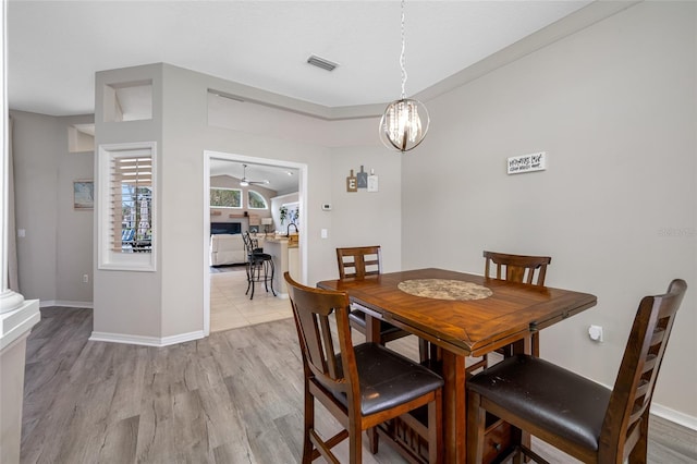 dining room featuring light wood-style floors, baseboards, visible vents, and ceiling fan with notable chandelier