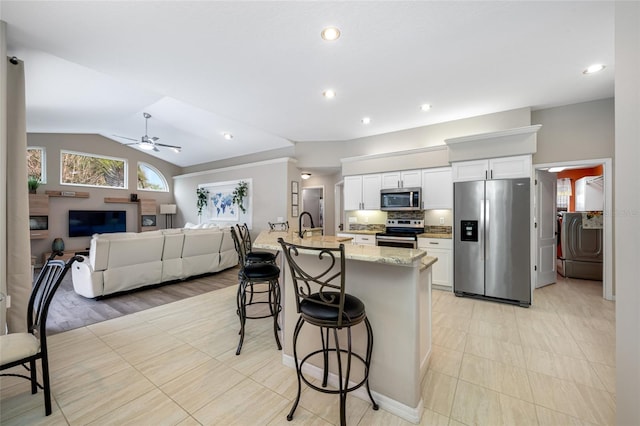 kitchen with white cabinets, lofted ceiling, washer / clothes dryer, a breakfast bar, and stainless steel appliances