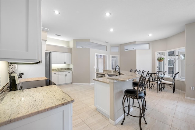 kitchen with light stone counters, electric range, a breakfast bar, a sink, and white cabinetry