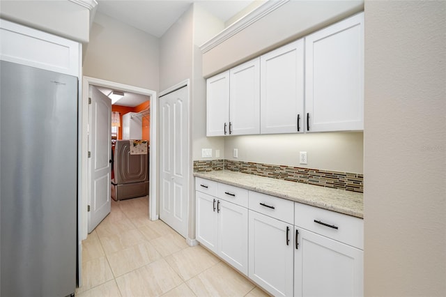 kitchen featuring light stone counters, freestanding refrigerator, white cabinets, and backsplash