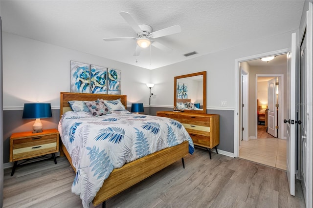 bedroom with a textured ceiling, wood finished floors, visible vents, baseboards, and a ceiling fan