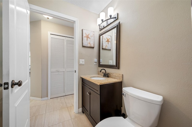 bathroom with a closet, toilet, vanity, baseboards, and tile patterned floors