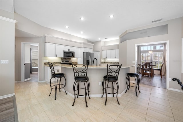 kitchen featuring stainless steel appliances, white cabinetry, a kitchen bar, and visible vents
