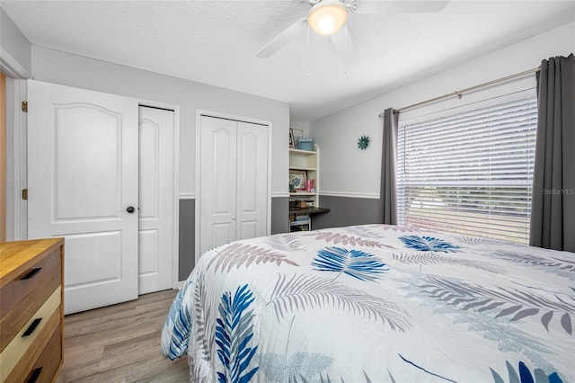 bedroom featuring ceiling fan, light wood-type flooring, and multiple closets