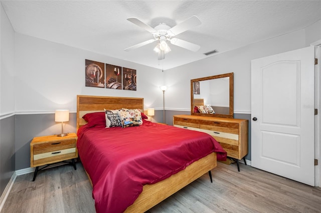 bedroom with wood finished floors, a textured ceiling, visible vents, a ceiling fan, and baseboards