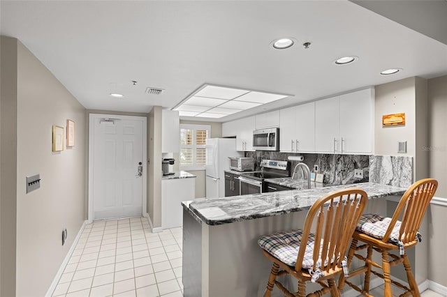 kitchen featuring visible vents, a breakfast bar, light stone counters, stainless steel appliances, and a peninsula