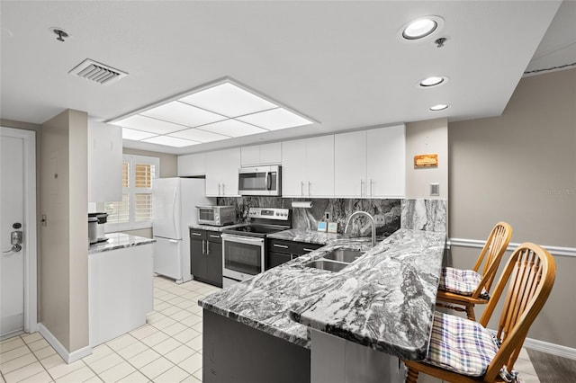 kitchen with visible vents, light stone counters, appliances with stainless steel finishes, a peninsula, and a sink