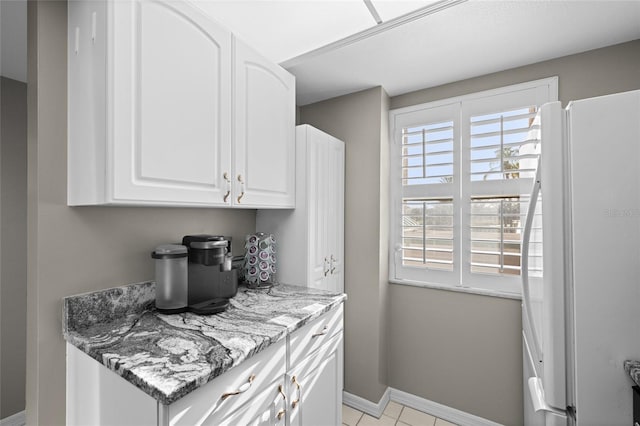 kitchen featuring freestanding refrigerator, white cabinets, light tile patterned floors, baseboards, and light stone countertops