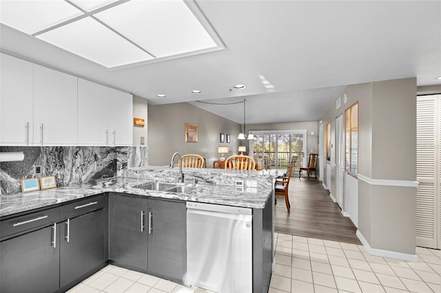 kitchen featuring a sink, white cabinetry, a peninsula, light tile patterned flooring, and dishwasher