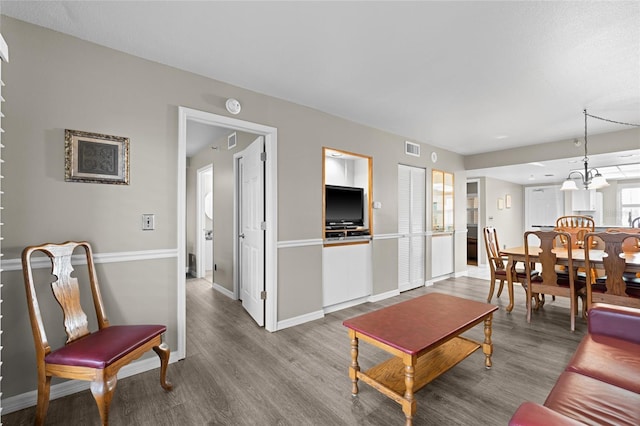 living area with wood finished floors, visible vents, a chandelier, and baseboards