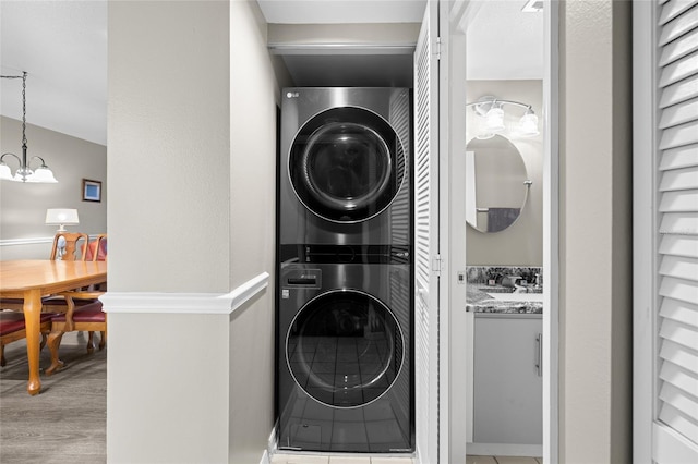 laundry room featuring laundry area, stacked washer / dryer, a notable chandelier, and light wood-type flooring