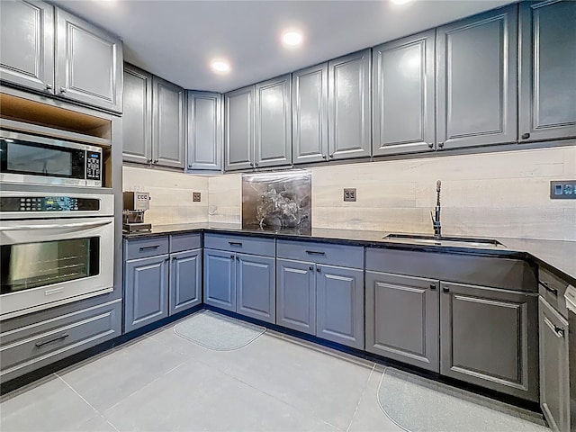 kitchen with light tile patterned floors, stainless steel appliances, dark countertops, decorative backsplash, and a sink