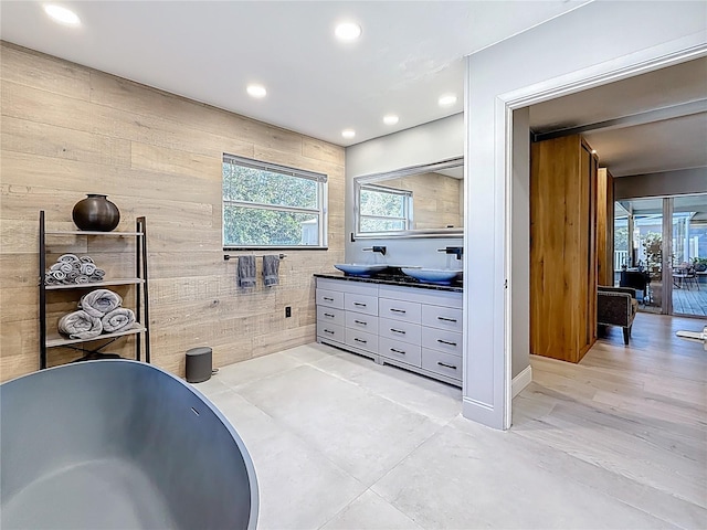 bathroom with double vanity, a freestanding tub, a sink, and recessed lighting