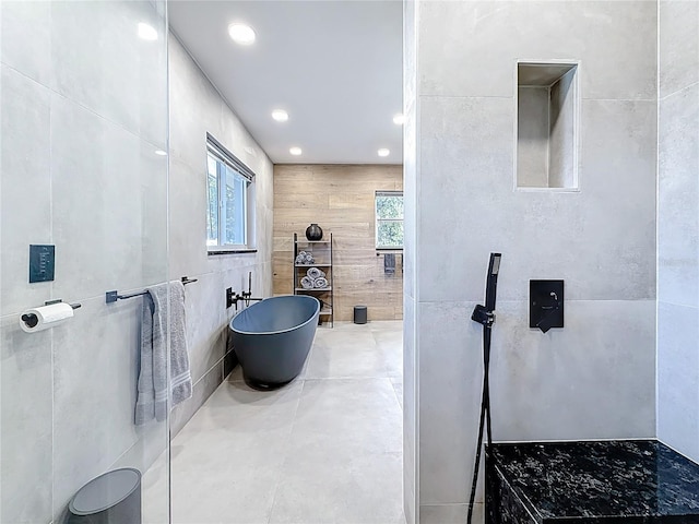 bathroom with recessed lighting, a freestanding tub, and tile walls