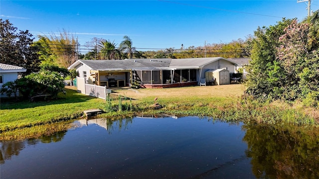 rear view of house featuring an outdoor structure, a water view, a sunroom, a lawn, and a shed