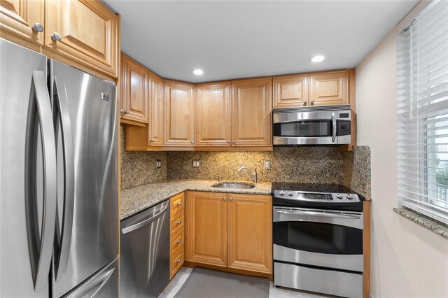 kitchen featuring backsplash, light stone countertops, appliances with stainless steel finishes, and a sink