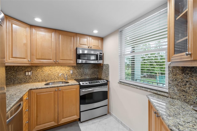 kitchen featuring light stone countertops, a sink, decorative backsplash, stainless steel appliances, and glass insert cabinets