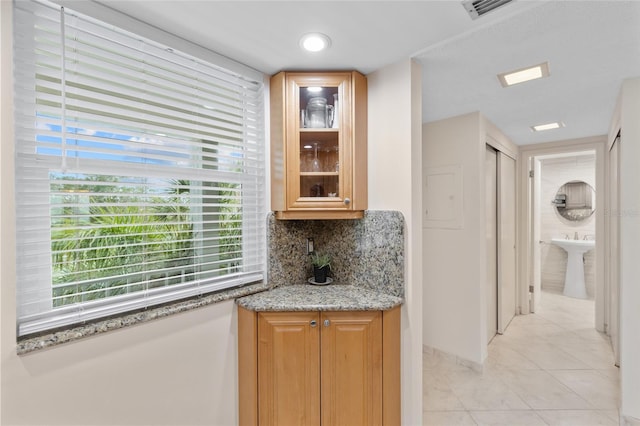 kitchen with light stone countertops, visible vents, light tile patterned flooring, decorative backsplash, and glass insert cabinets