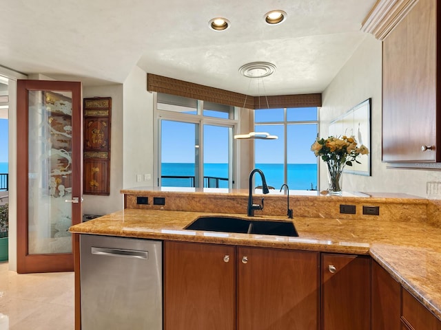 kitchen featuring light stone countertops, a water view, dishwasher, brown cabinetry, and a sink