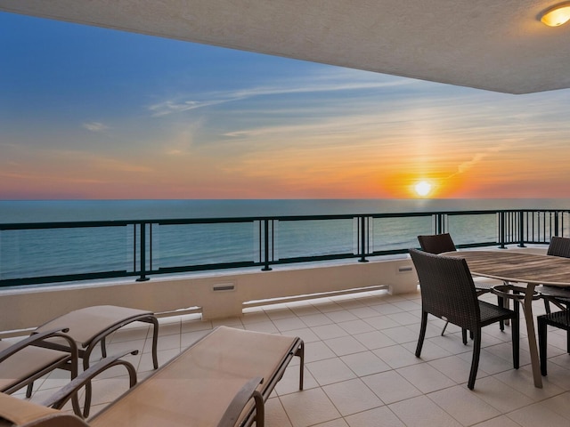 patio terrace at dusk featuring a water view and a balcony