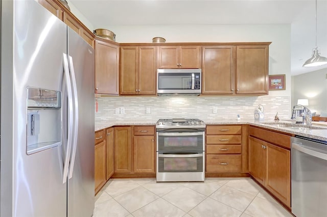 kitchen with brown cabinetry, light stone counters, a sink, stainless steel appliances, and backsplash