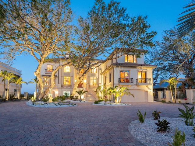 mediterranean / spanish-style house featuring an attached garage, a balcony, decorative driveway, and stucco siding